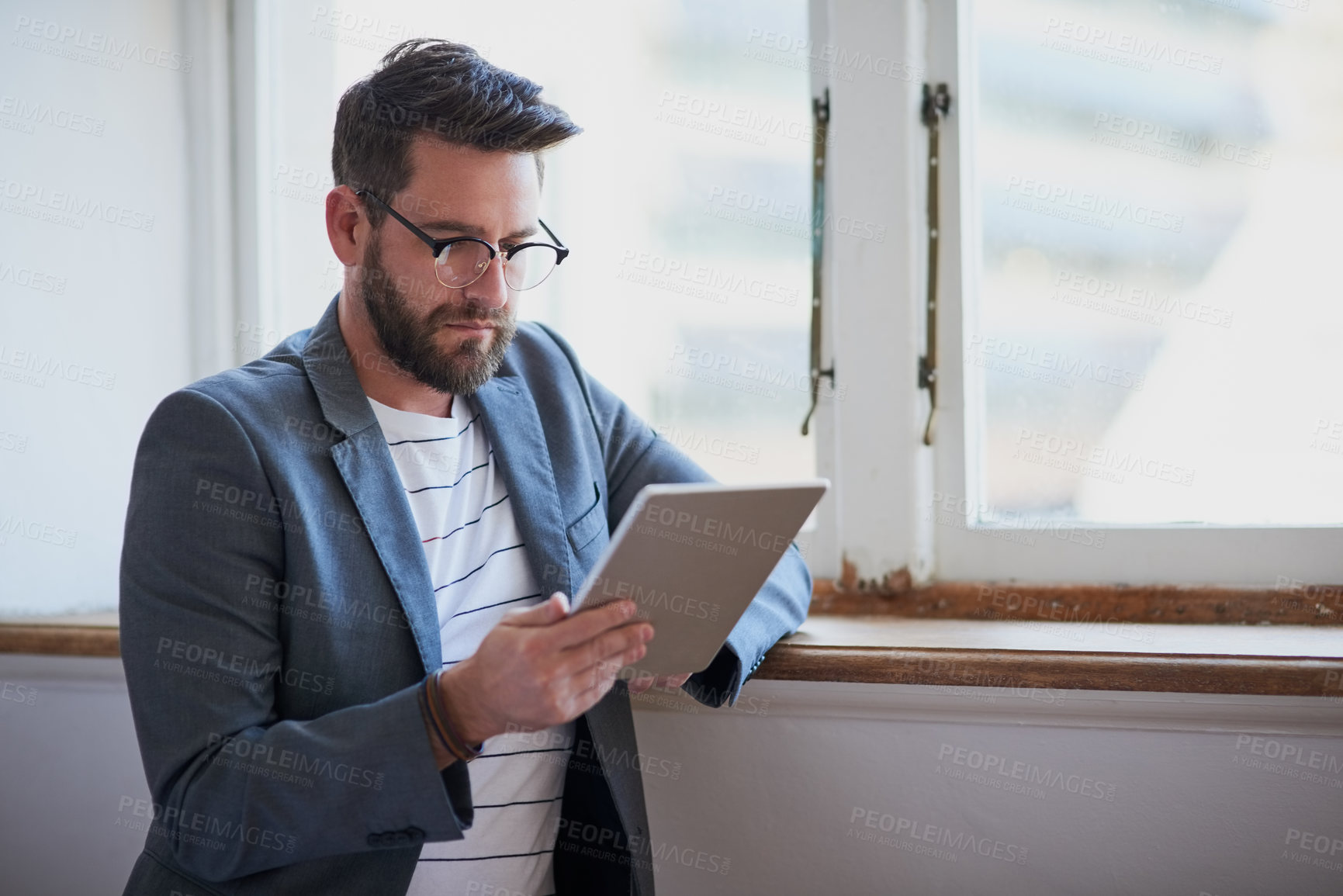 Buy stock photo Cropped shot of a handsome young businessman working on a tablet while standing by his bedroom window