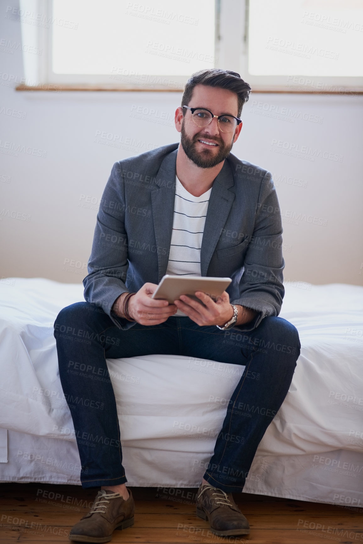 Buy stock photo Full length portrait of a handsome young businessman working on a tablet while sitting on his bed at home