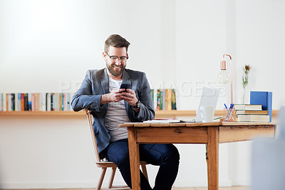Buy stock photo Cropped shot of a handsome young businessman sending a text message while sitting in the home office