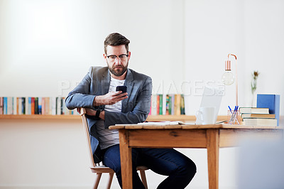 Buy stock photo Cropped shot of a handsome young businessman sending a text message while sitting in the home office