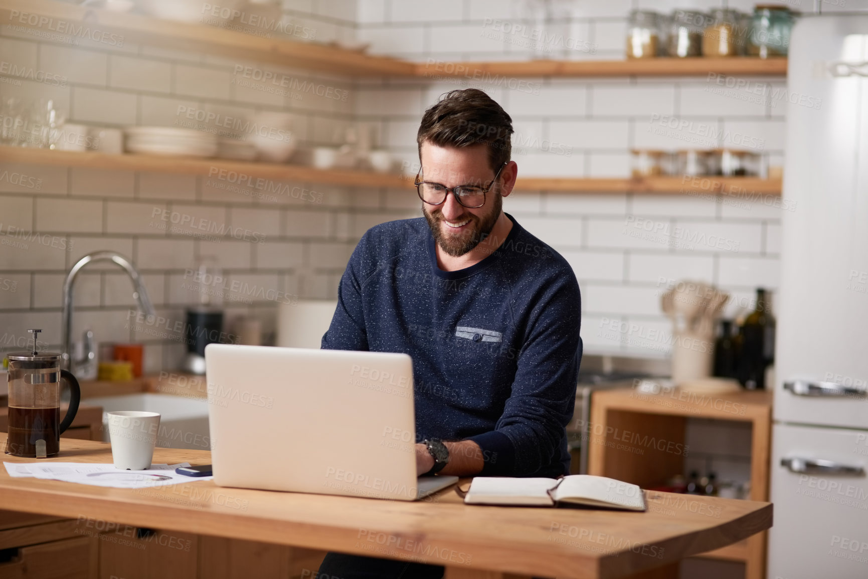 Buy stock photo Cropped shot of a handsome young businessman working on his laptop while sitting in the kitchen at home