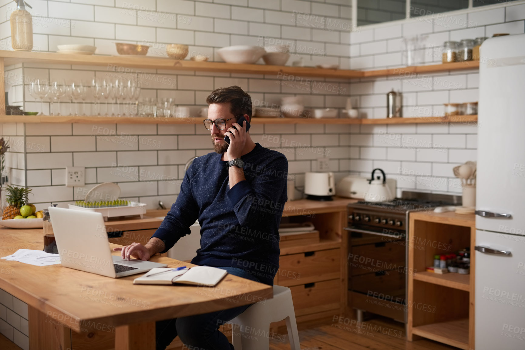 Buy stock photo Cropped shot of a handsome young businessman making a phonecall while sitting in the kitchen at home