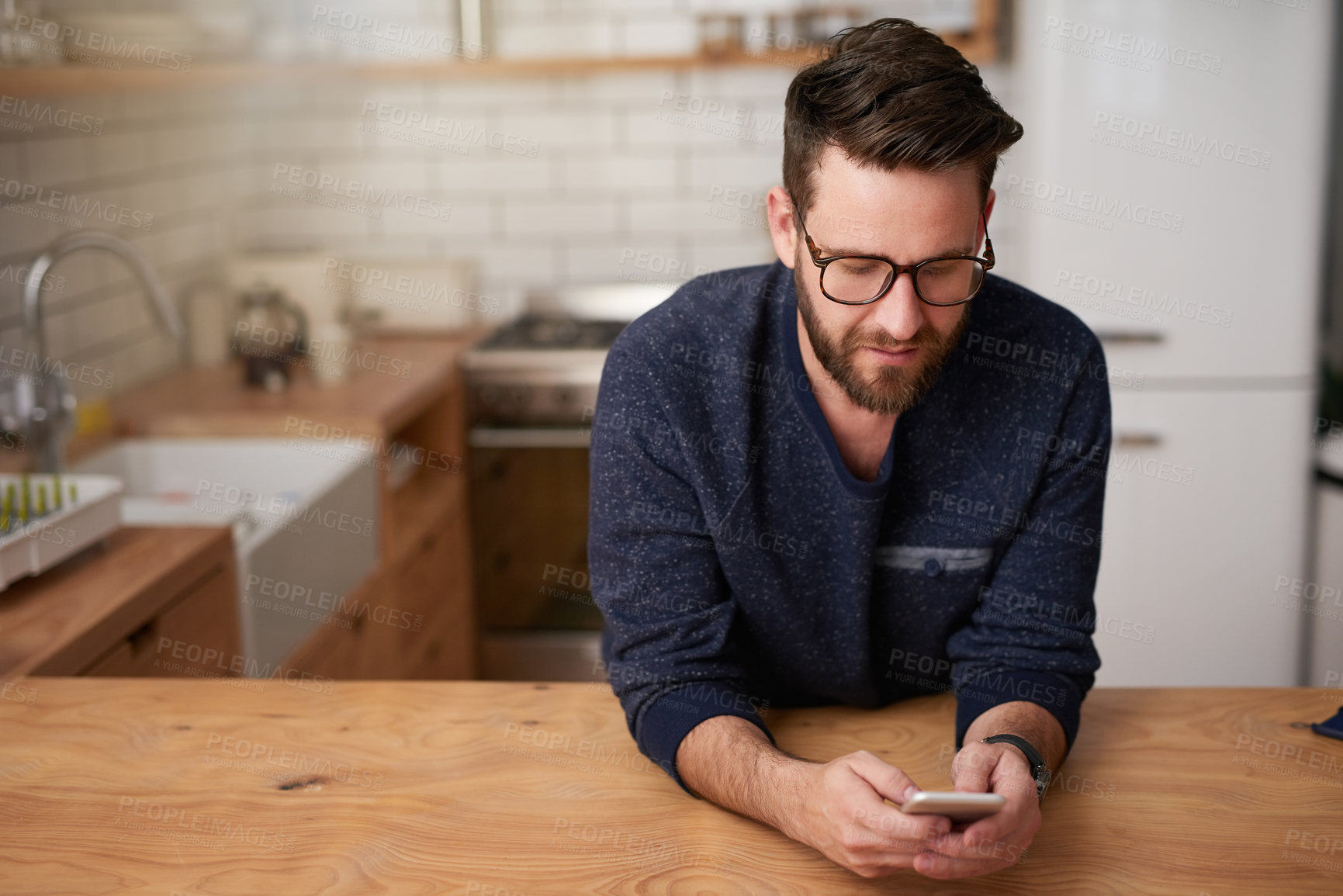 Buy stock photo Cropped shot of a handsome young man sending a text message while standing in the kitchen at home