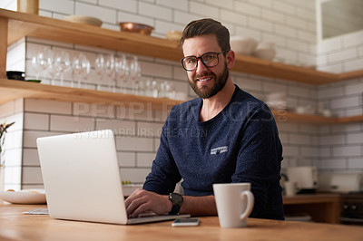 Buy stock photo Cropped portrait of a handsome young businessman working on his laptop while sitting in the kitchen at home