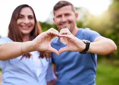 Buy stock photo Portrait of a cheerful young couple forming a heart together with their hands while standing outside in a park during the day