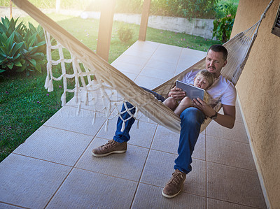 Buy stock photo Shot of a father and his little daughter using a digital tablet while relaxing on a hammock outdoors