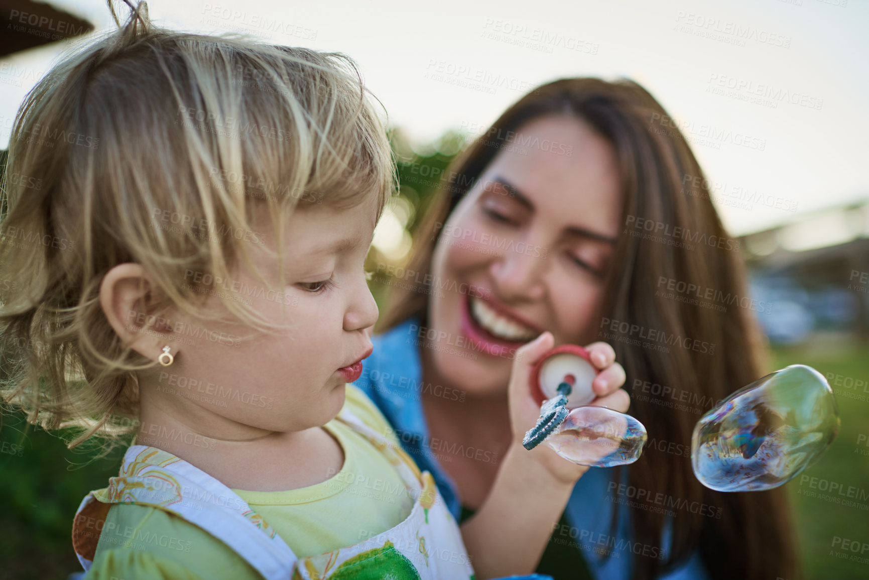 Buy stock photo Mom, girl and blowing bubbles in garden with care, learning and happy with support, love and bonding. Family, mother and daughter for summer with soap, smile and connection in backyard in Spain