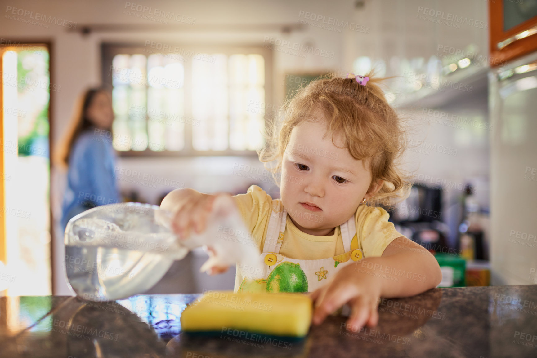 Buy stock photo Shot of a little girl holding a bottle of cleaning detergent with her mother in the background at home