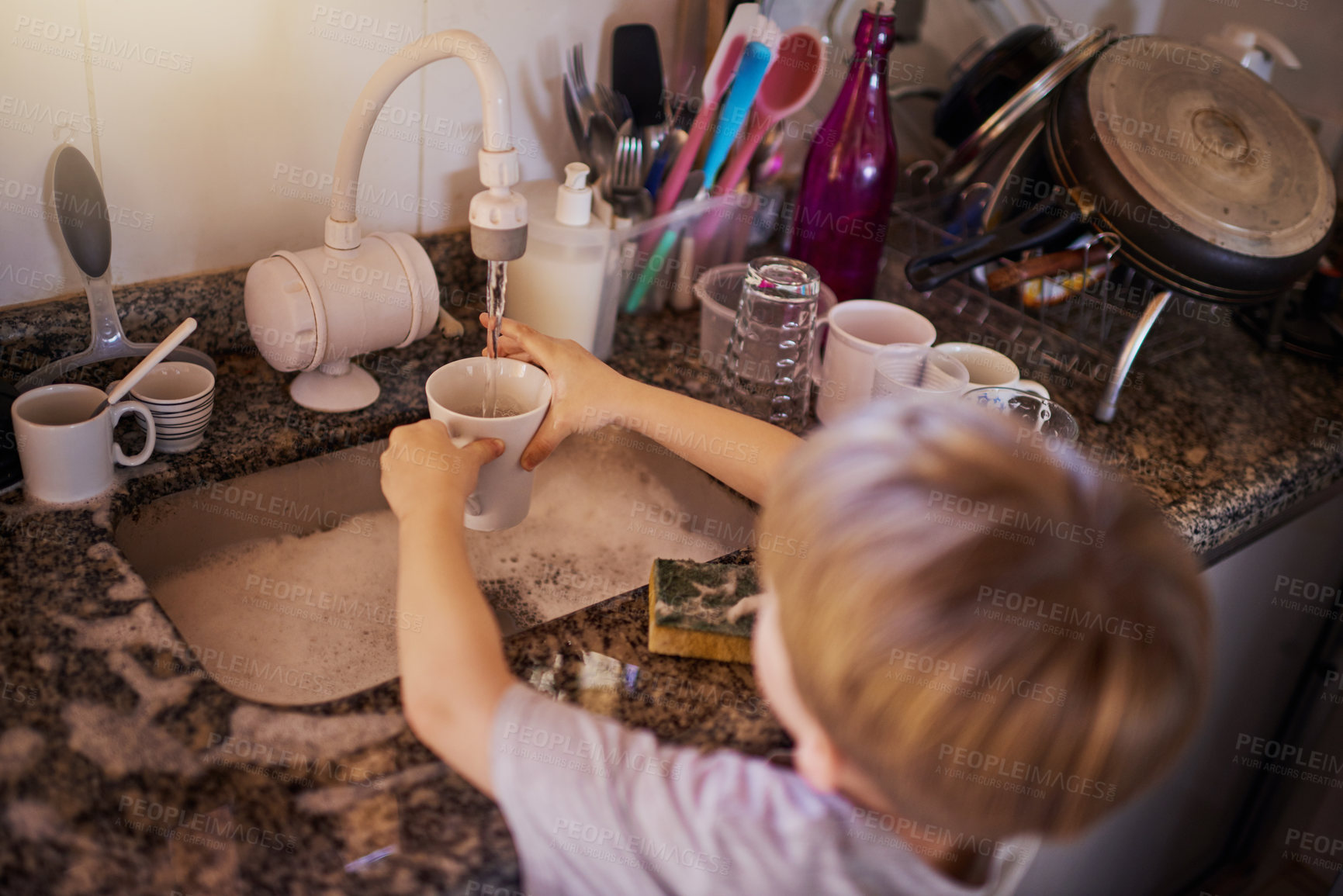 Buy stock photo High angle shot of a little boy washing dishes in the kitchen at home
