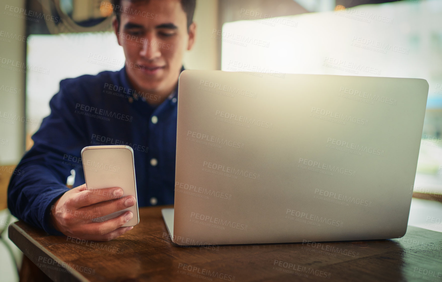 Buy stock photo Shot of a young man using a mobile phone and laptop in a cafe
