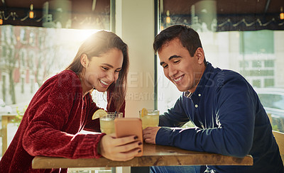 Buy stock photo Shot of a young man and woman using a mobile phone together on a date at a coffee shop