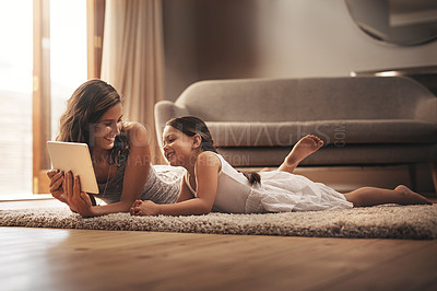 Buy stock photo Shot of a young woman and her adorable daughter using a digital tablet while relaxing on the floor at home