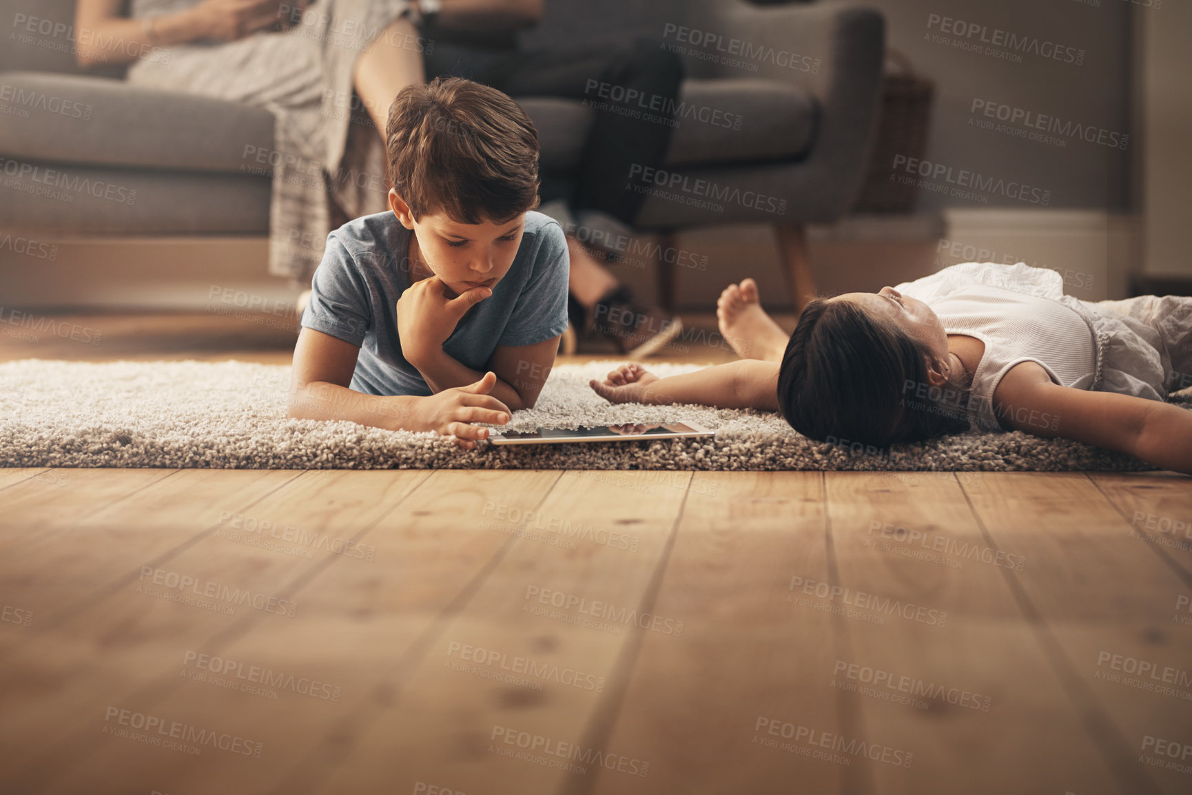 Buy stock photo Shot of an adorable brother and sister using a digital tablet at home with their parents in the background