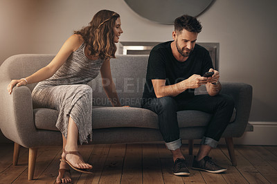 Buy stock photo Shot of a young woman looking at what her husband is doing on his phone