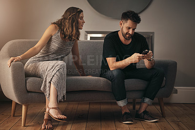 Buy stock photo Shot of a young woman looking at what her husband is doing on his phone