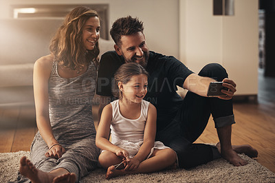 Buy stock photo Shot of a happy young family taking a selfie together at home