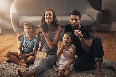 Buy stock photo Shot of a young family relaxing on the floor and watching movies together at home