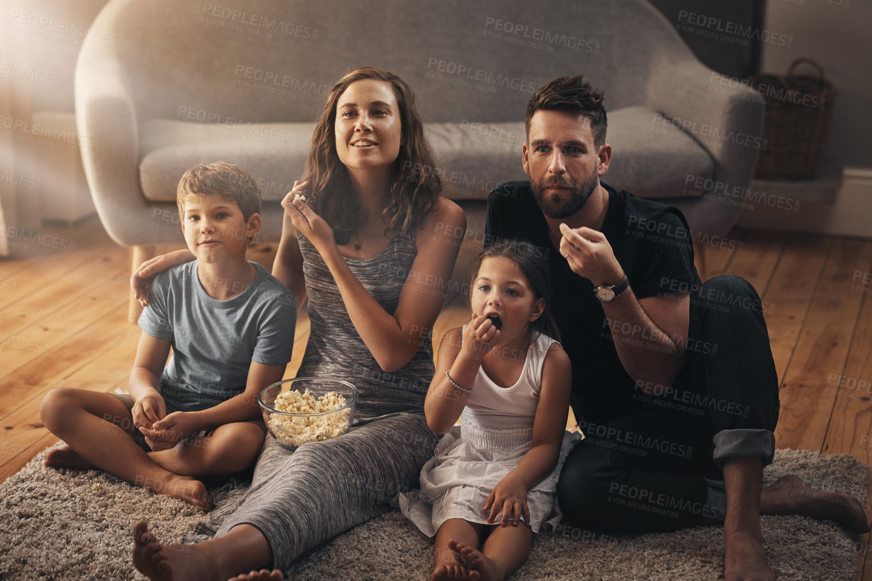 Buy stock photo Shot of a young family relaxing on the floor and watching movies together at home