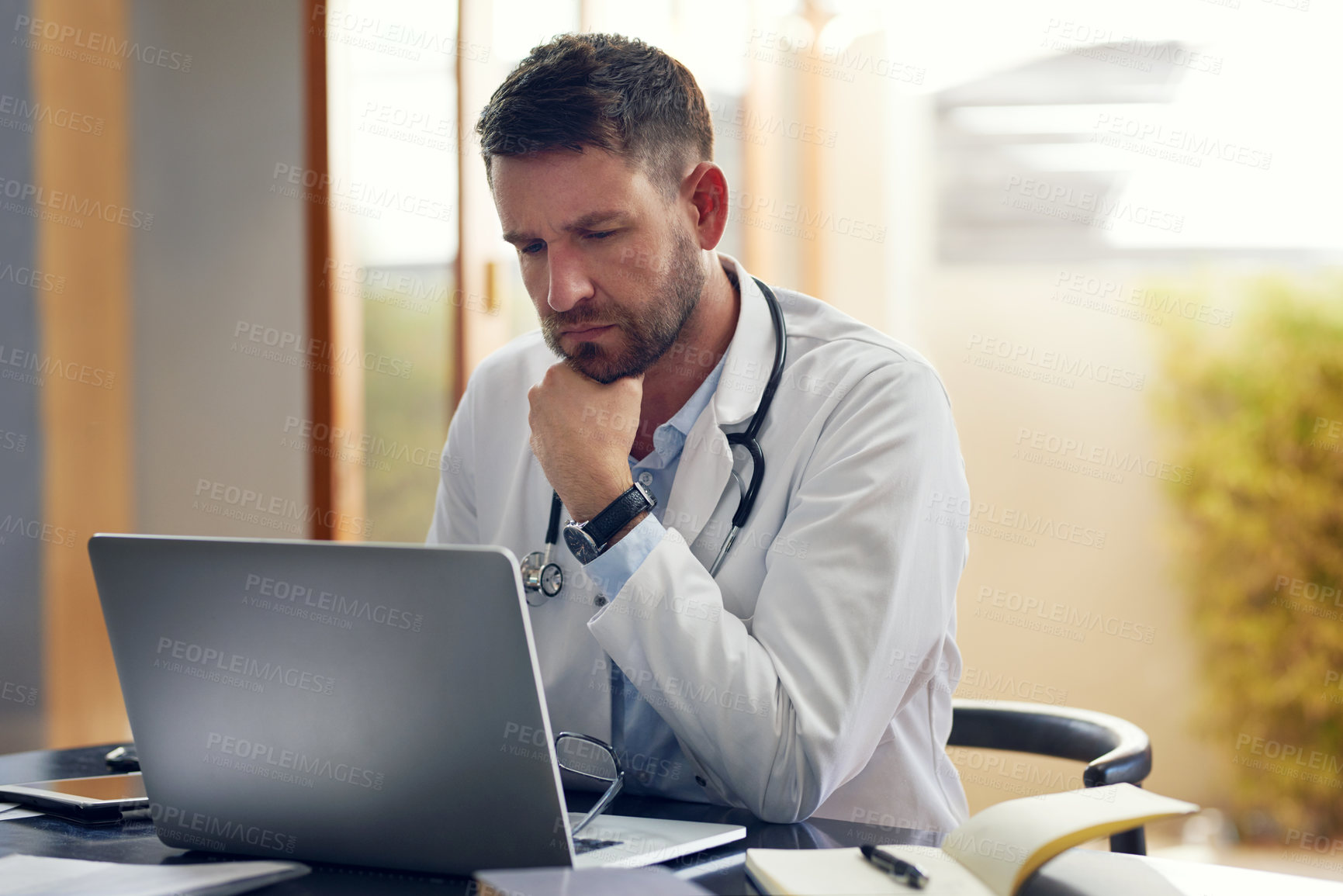 Buy stock photo Cropped shot of a handsome male doctor working on his laptop while sitting in his office