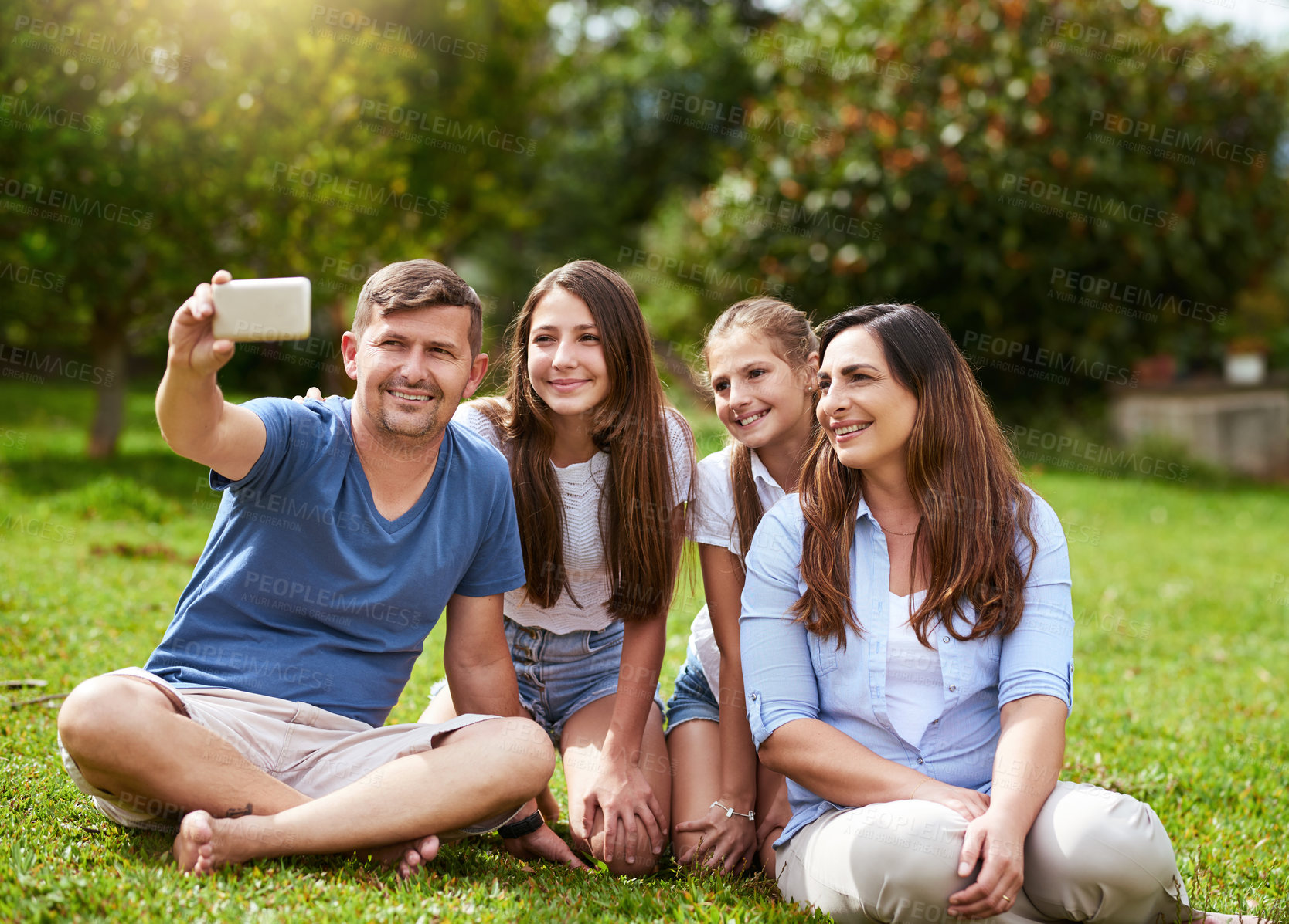 Buy stock photo Shot of a cheerful family seated in a park while taking a self portrait together outside during the day