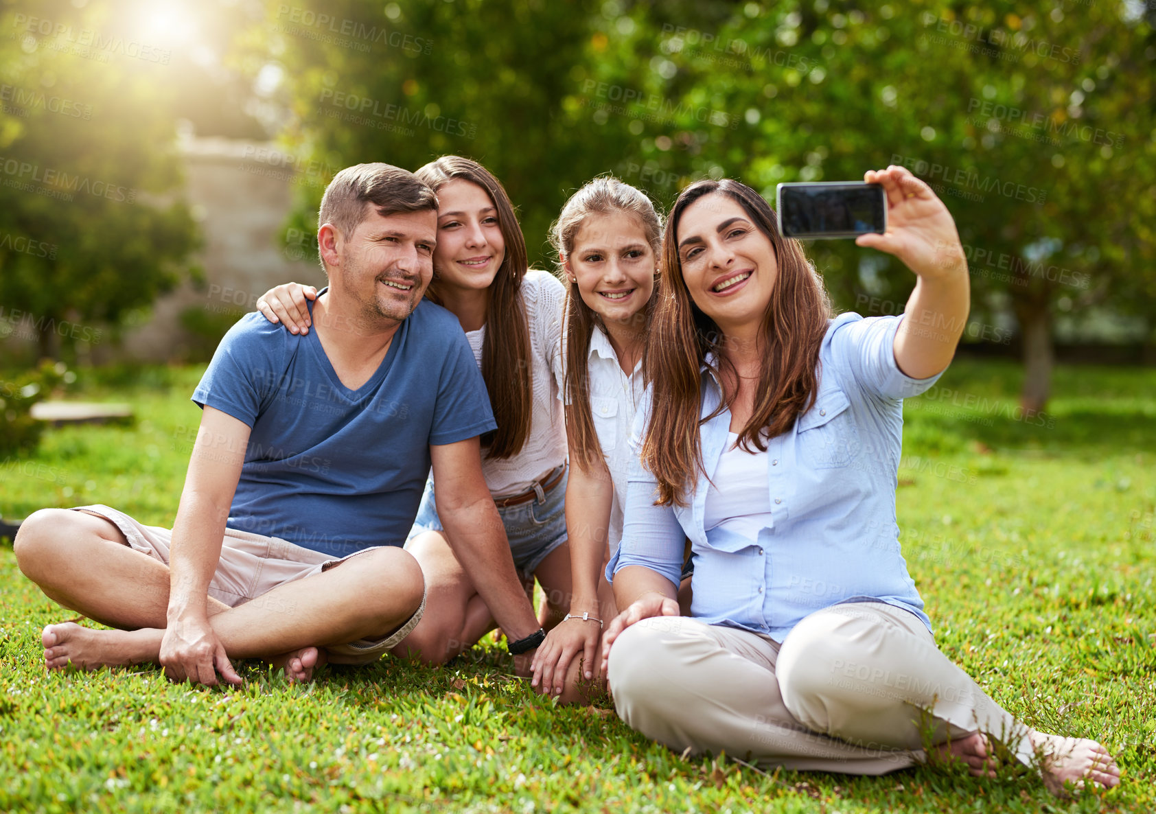 Buy stock photo Shot of a cheerful family seated in a park while taking a self portrait together outside during the day