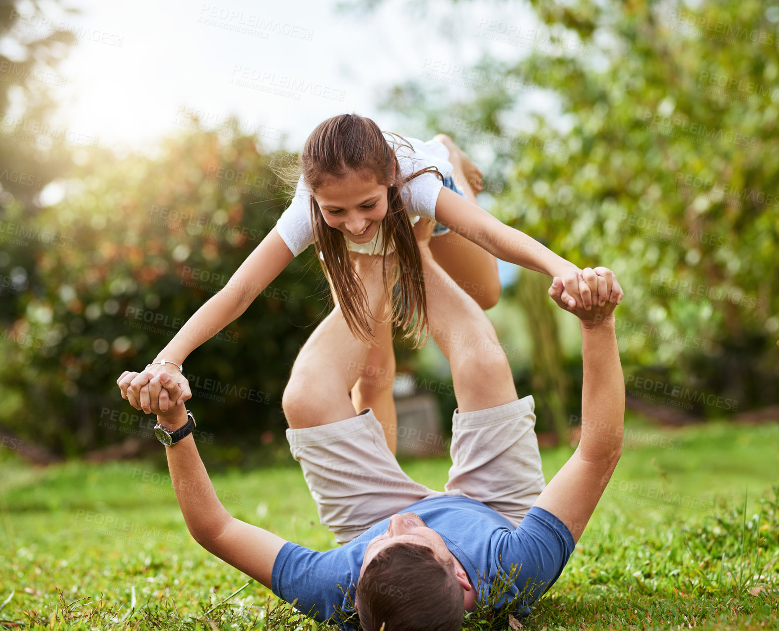 Buy stock photo Shot of a father lifting up his daughter with his legs while lying on the grass of a park outside during the day