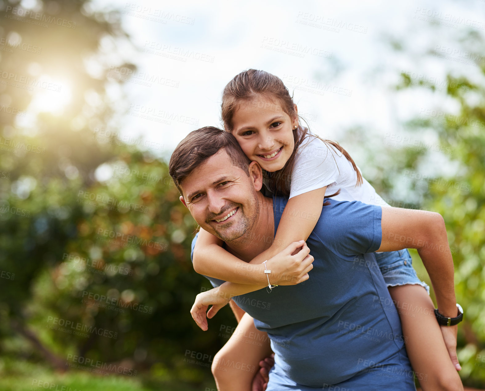Buy stock photo Portrait of a cheerful young man giving his daughter a piggyback ride outside in a park during the day