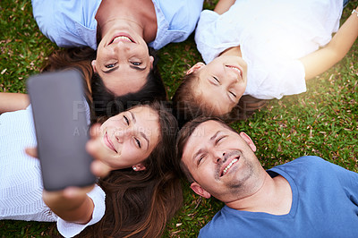 Buy stock photo Portrait of a cheerful family lying on the ground while taking a self portrait together outside in a park during the day