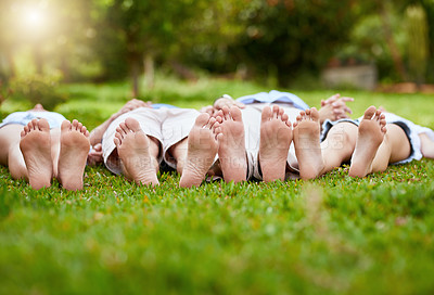 Buy stock photo Shot of a group of unrecognizable people lying on grass with their feet up outside in a park  during the day