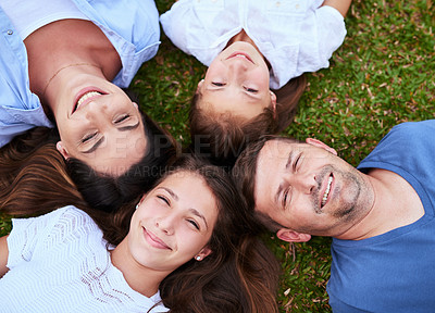 Buy stock photo Portrait of a cheerful family lying on the ground together outside in a park during the day