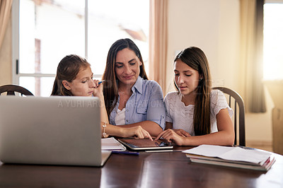 Buy stock photo Shot of two cheerful young girls doing homework around a table while getting help from their mother at home during the day