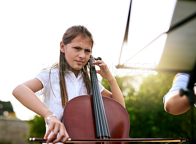 Buy stock photo Shot of a determined young girl playing the cello while standing in the backyard of her home during the day