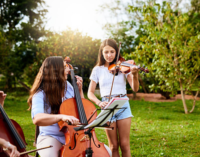 Buy stock photo Shot of a determined young mother and daughter playing classical string instruments together in their backyard at home during the day