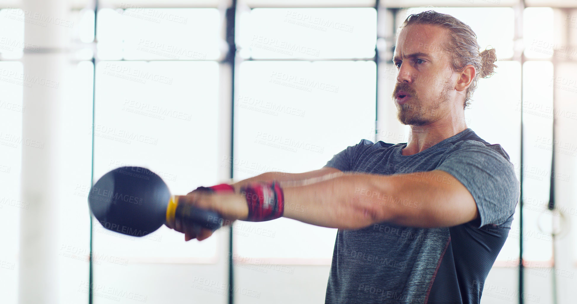Buy stock photo Shot of a young man working out with kettle bells in a gym