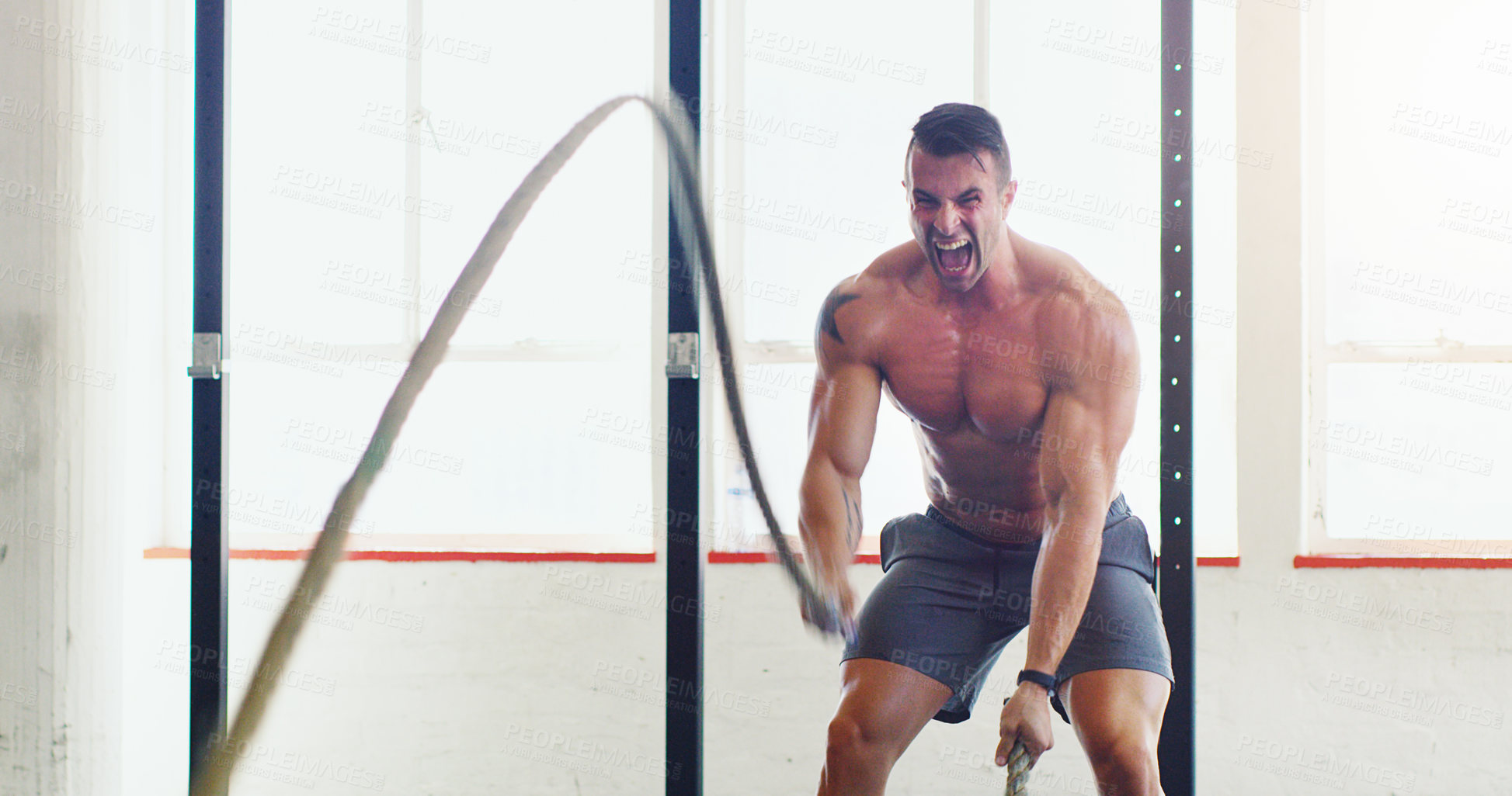 Buy stock photo Shot of a young man working out with battle ropes in a gym