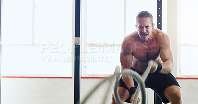 Buy stock photo Shot of a young man working out with battle ropes in a gym