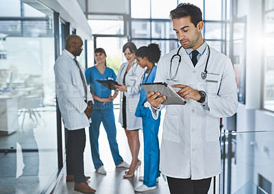 Buy stock photo Shot of a young doctor using a digital tablet in a hospital with his colleagues in the background