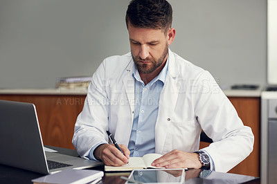 Buy stock photo Cropped shot of a handsome male doctor writing in his diary while sitting in his office