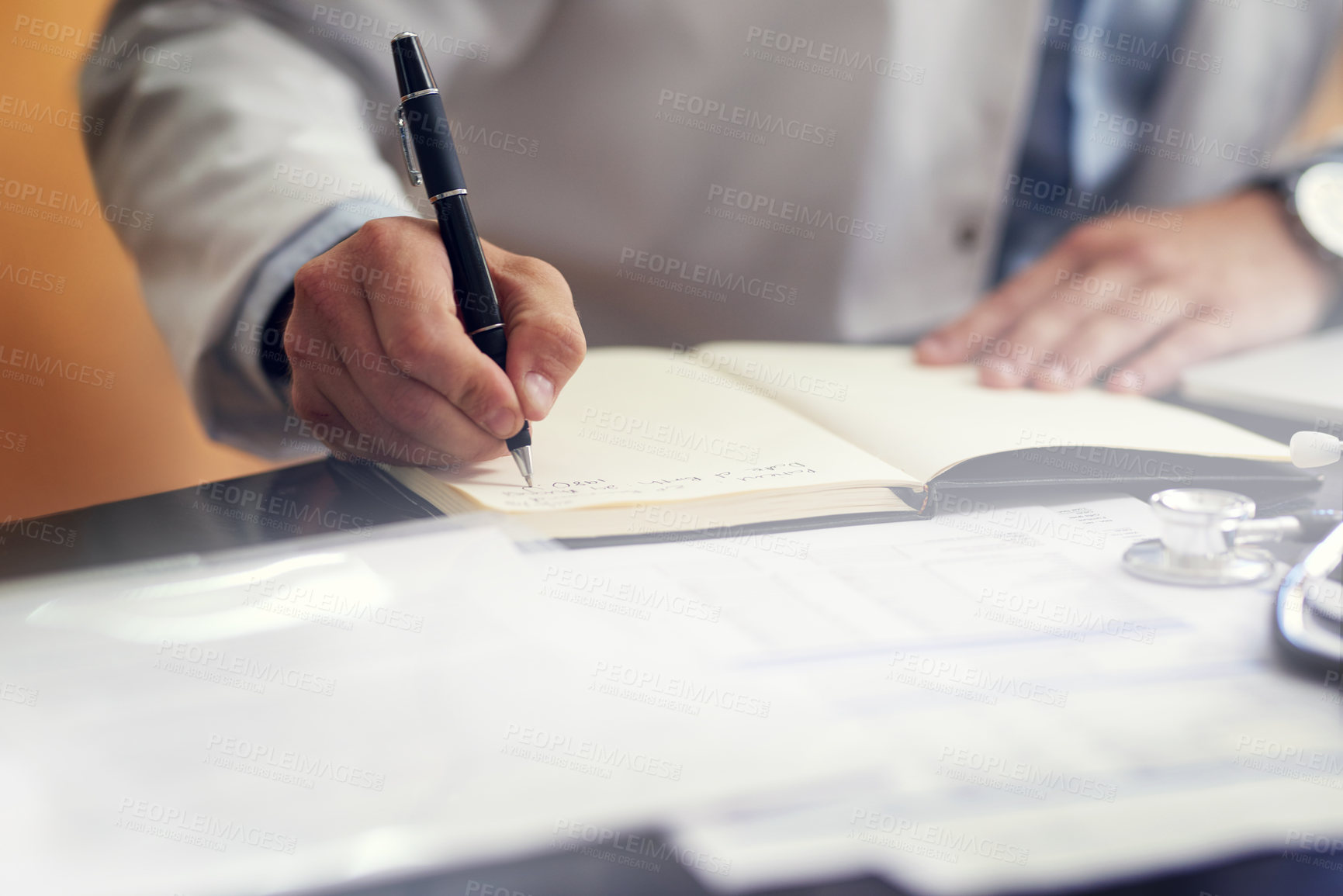 Buy stock photo Cropped shot of an unrecognizable male doctor writing in his diary while sitting in his office