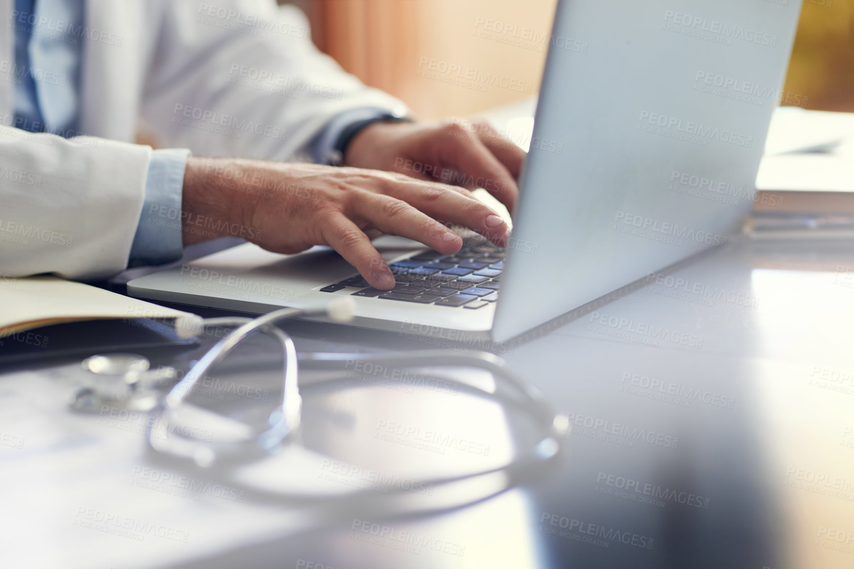 Buy stock photo Cropped shot of an unrecognizable male doctor working on his laptop while sitting in his office