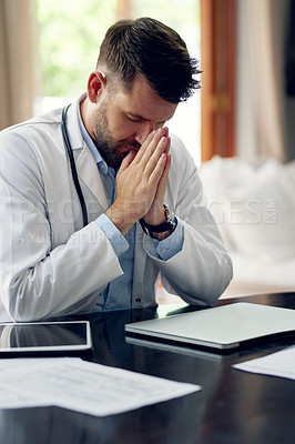 Buy stock photo Cropped shot of a handsome male doctor praying while sitting in his office
