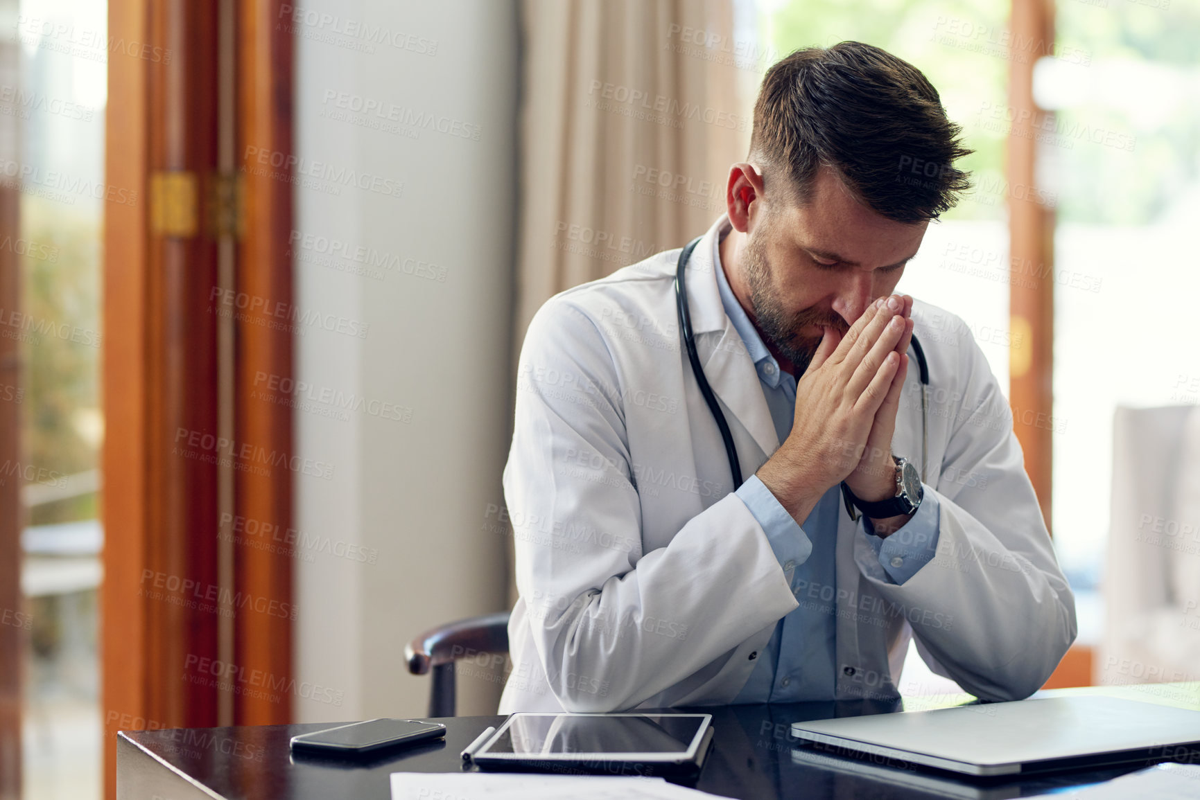 Buy stock photo Cropped shot of a handsome male doctor praying while sitting in his office