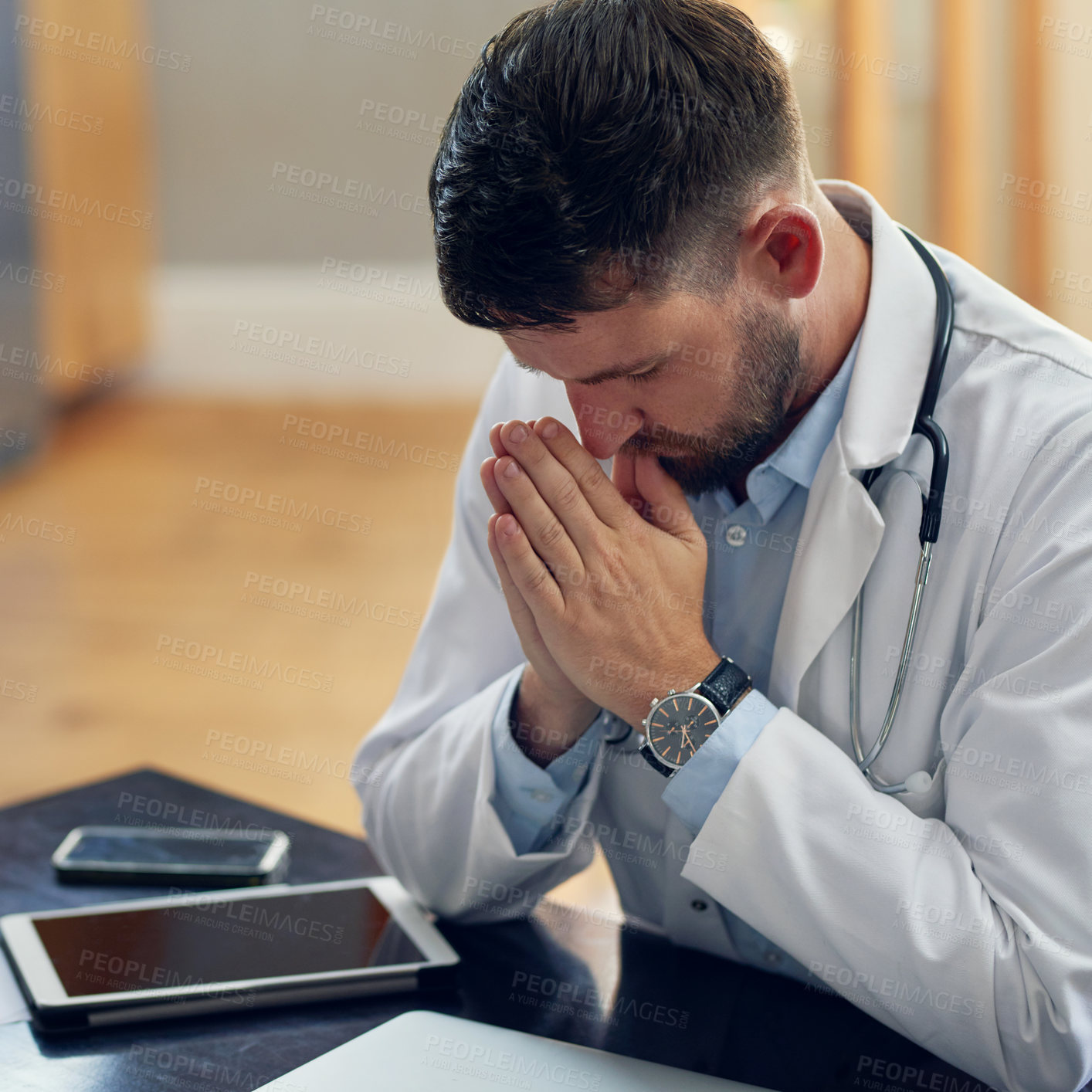 Buy stock photo High angle shot of a handsome male doctor praying while sitting in his office