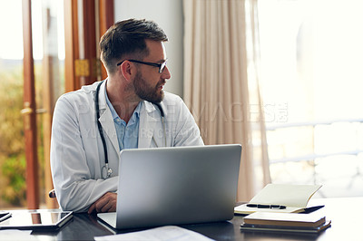 Buy stock photo Cropped shot of a handsome male doctor working on his laptop while sitting in his office