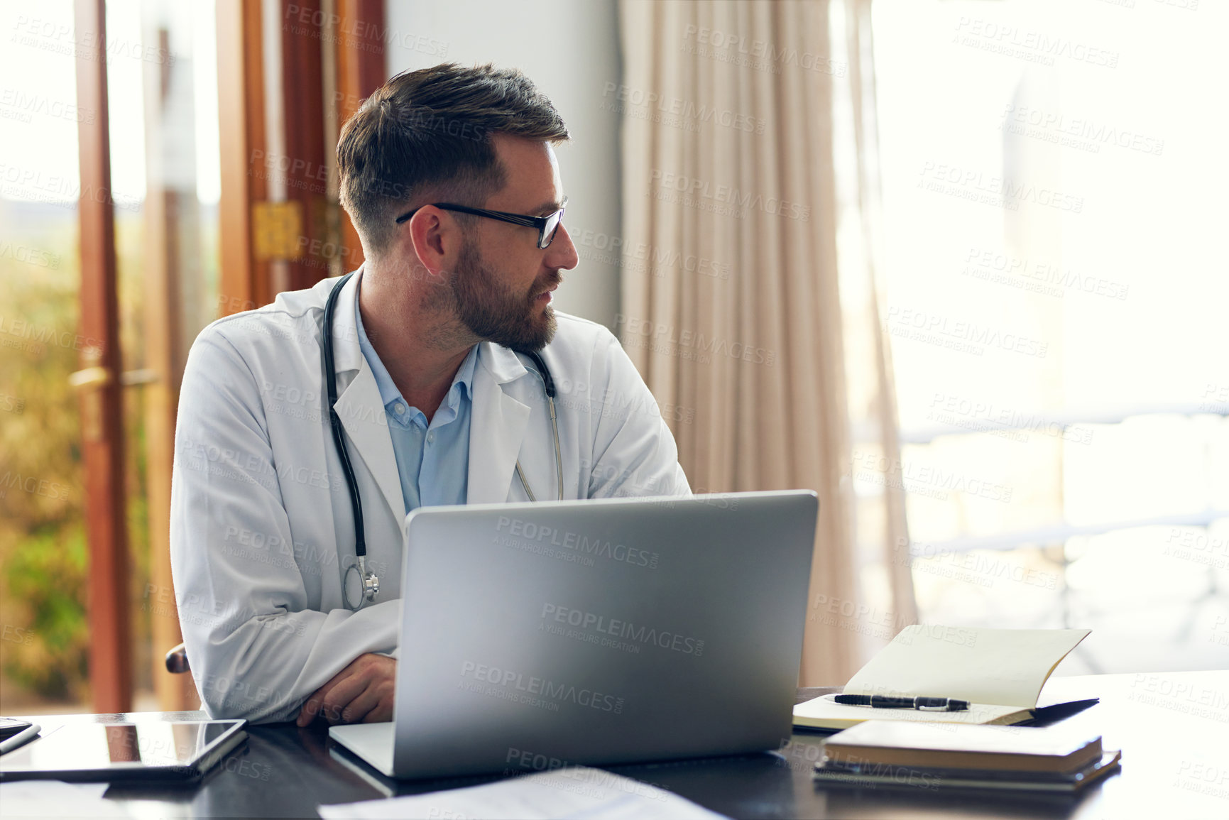 Buy stock photo Cropped shot of a handsome male doctor working on his laptop while sitting in his office