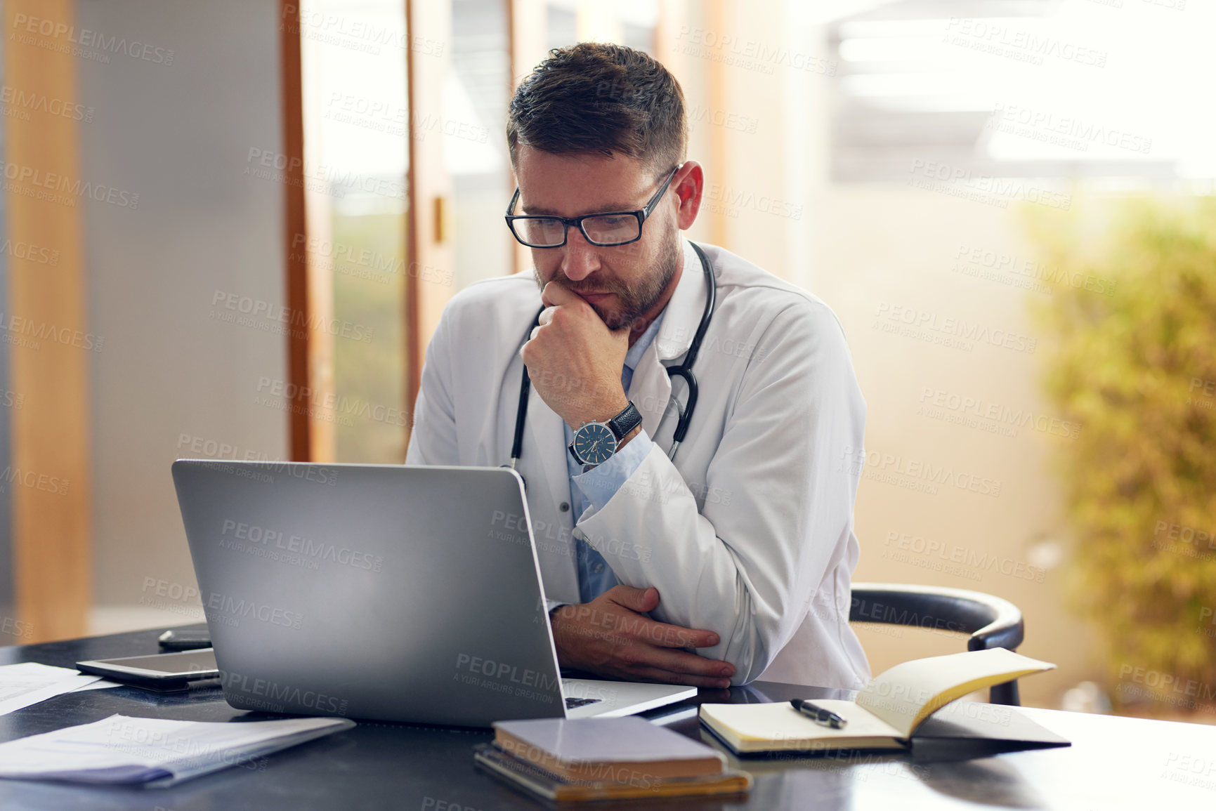 Buy stock photo Cropped shot of a handsome male doctor working on his laptop while sitting in his office