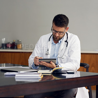 Buy stock photo Cropped shot of a handsome male doctor working on his tablet while sitting in his office