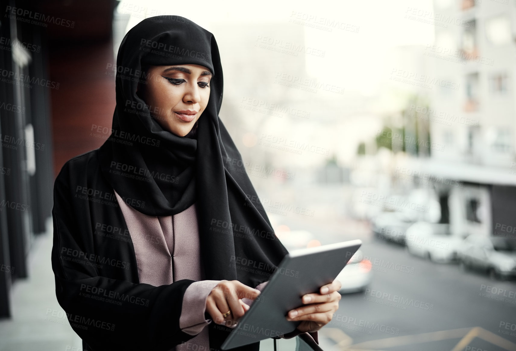 Buy stock photo Cropped shot of an attractive young businesswoman dressed in Islamic traditional clothing using a tablet while standing on her office balcony