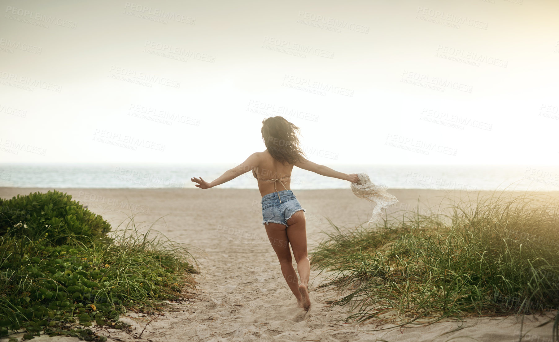 Buy stock photo Rearview shot of a happy young woman enjoying a day at the beach