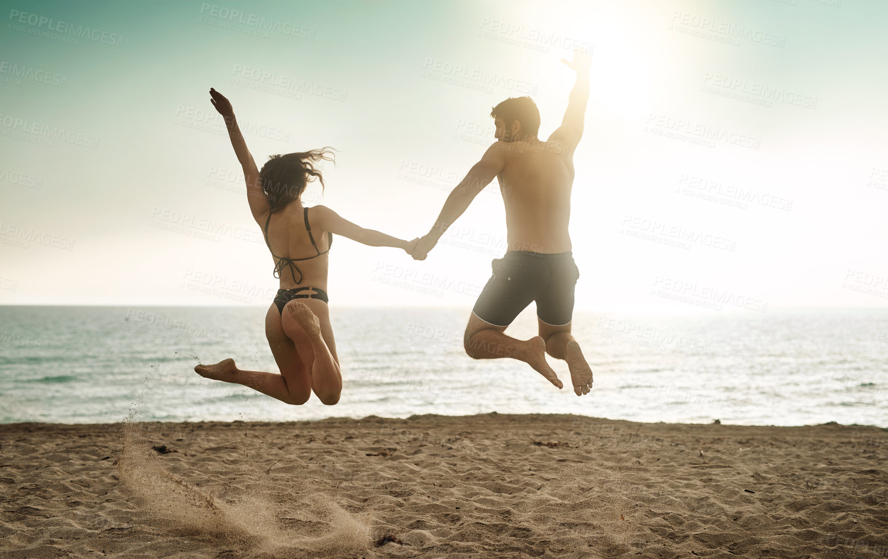 Buy stock photo Rearview shot of a young couple jumping into mid-air at the beach